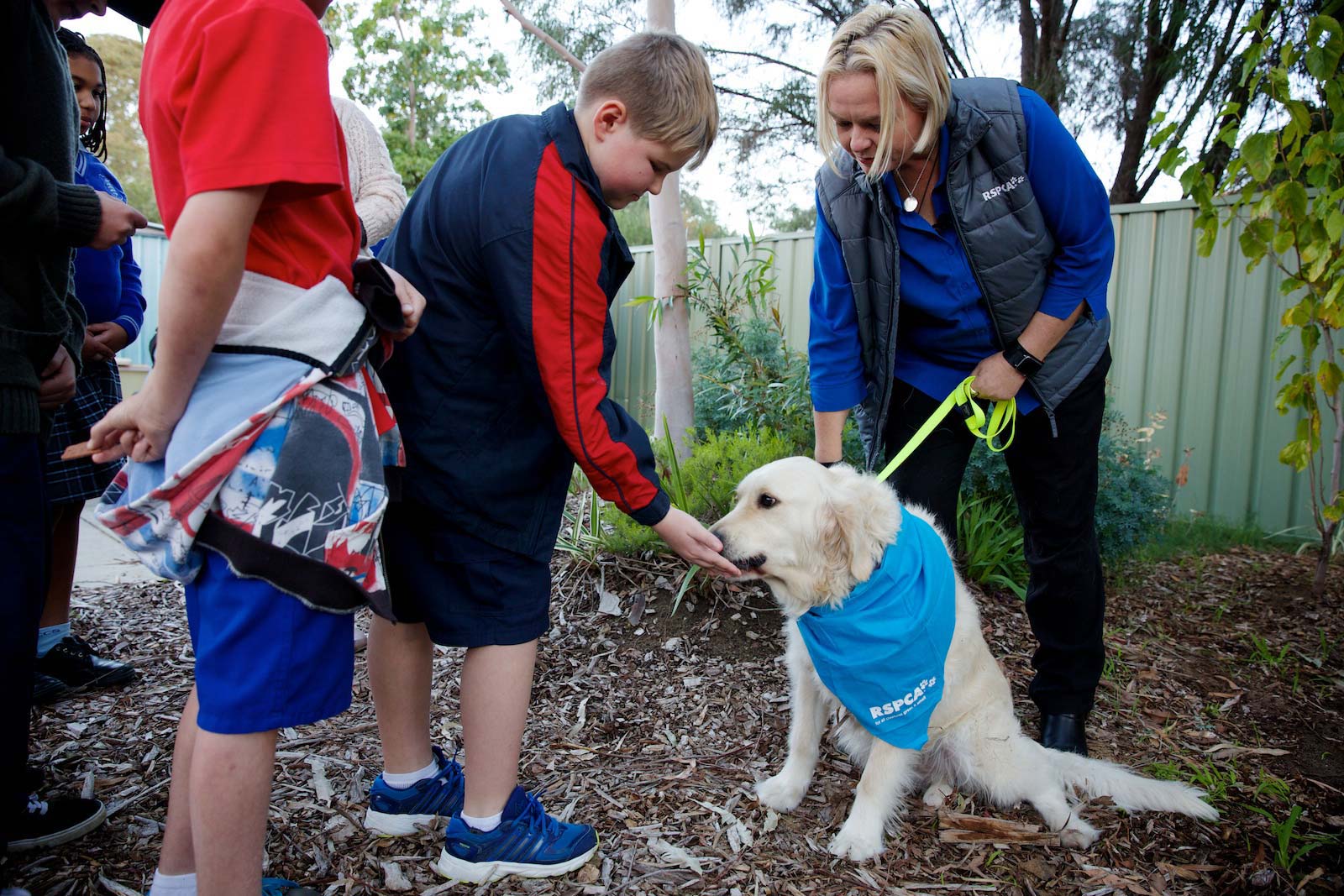 An adult woman holding a dog on a lead in front of a group of children